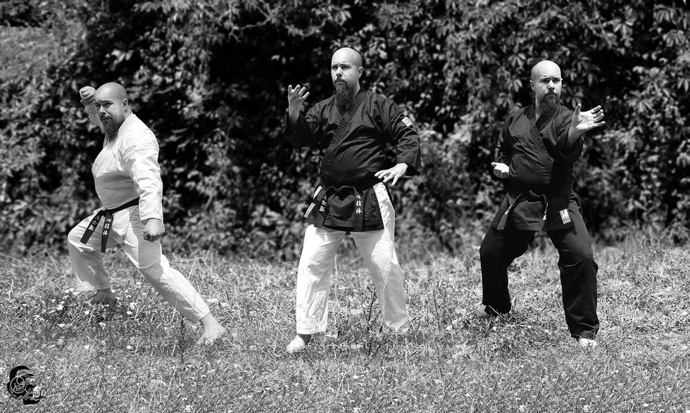 Trois hommes pratiquent les arts martiaux dans un jardin, vêtus de kimonos, en noir et blanc.