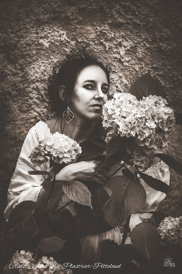 Femme près de fleurs avec regard direct, Isa. Reflets De Fawn, nature et élégance.