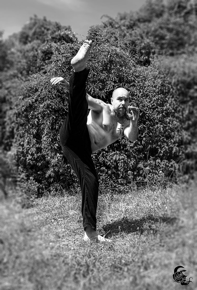 Homme musclé réalise un grand écart, extérieur, en noir et blanc, contre nature.