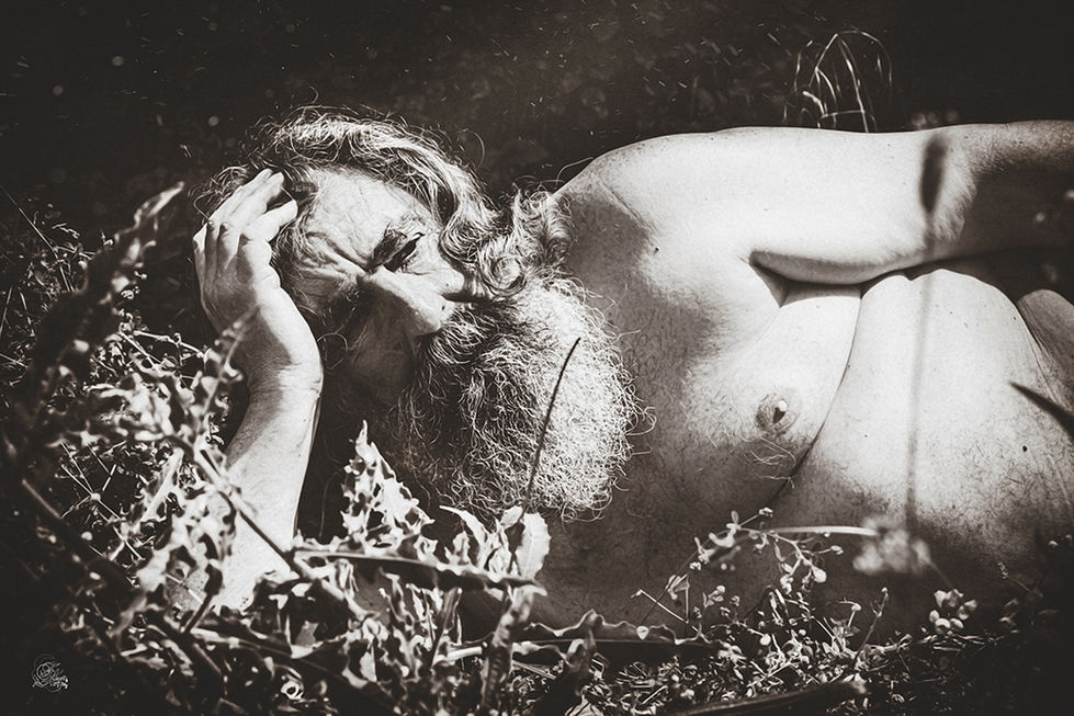 Un homme nu allongé, pensif, parmi la végétation, son visage est visible.