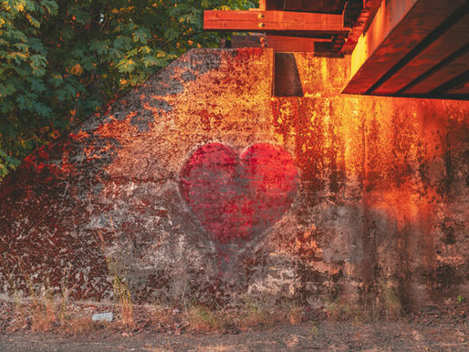 Faded red heart painted on an old wall; tree foliage on the left