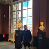 Person steht in einem Museum mit hohen Fenstern und Skulpturen im Hintergrund.