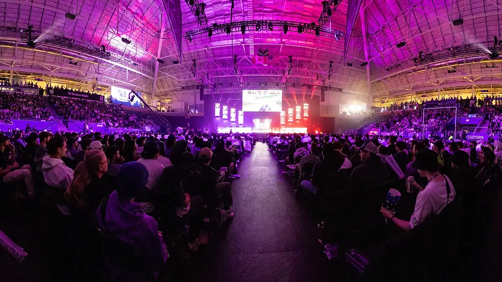 Crowd watches an esports event at The Aud Kitchener, in a large, purple-lit arena with a high ceiling. Screens display Call of Duty visuals. Emotions are excited and engaged.