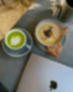 Green matcha latte with heart art, mushroom soup with garnish, bread on dark table. Silver laptop and containers in background. Cozy mood.