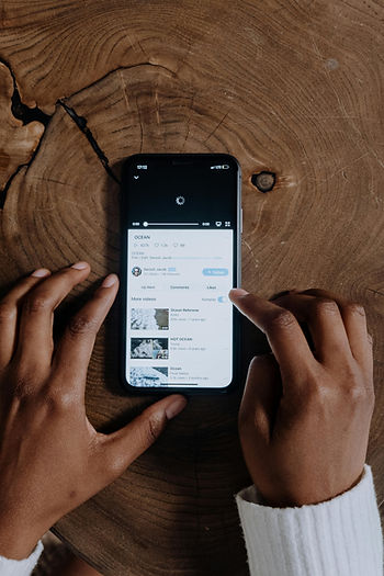 Hands holding a phone with a loading video titled "OCEAN" on a wooden table. User browsing and liking videos. Calm mood.
