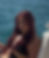 A woman with long red hair sits on a boat, wearing a black outfit with gold accents. The mood is relaxed, with the ocean in the background.