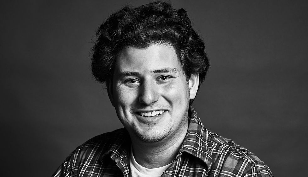 Smiling person with curly hair in a plaid shirt against a plain background, conveying a friendly and relaxed mood. Black and white.