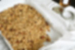 Toasted granola with pecans on a baking tray with parchment paper, set on a white cloth. Nearby are a jar with a lid and a bottle.