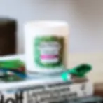 A white candle with a green leafy design and "Pot-Pourri" label sits on art books beside a green lighter. Calm, cozy setting.