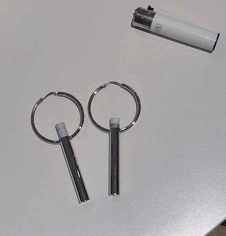 Silver metallic keyrings with cylindrical attachments and a white lighter on a smooth white surface. Simple, minimalist setup.