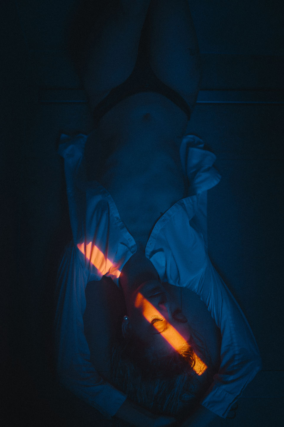 Portrait von Christin in der Dusche.  Es ist ein Boudoir-Foto in blauem Blitz-Licht mit orangem Spalt. Sie liegt, nur bekleidet mit einer offenen Blouse und einem Tanga.