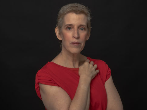 Studio professional headshot of a woman wearing a red dress photographed against a dark background in Boston