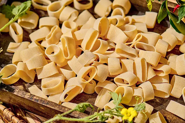 Miniatura: Calamarata selected durum wheat pasta rings on wooden tray, bronze-drawn porous texture close-up