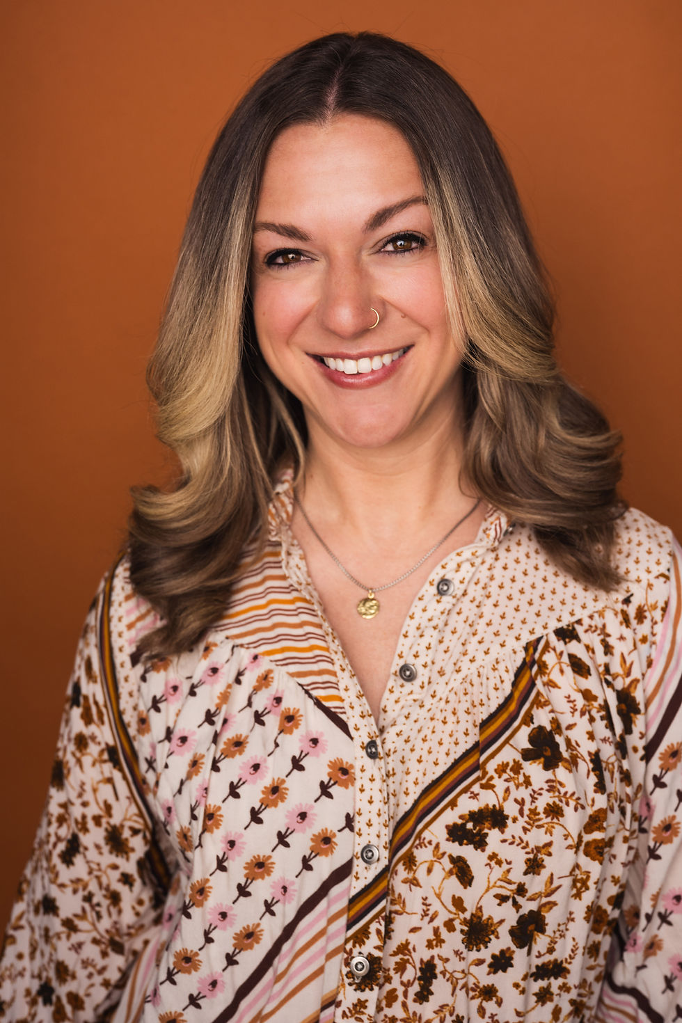 Smiling woman with wavy blonde hair in a floral blouse.
