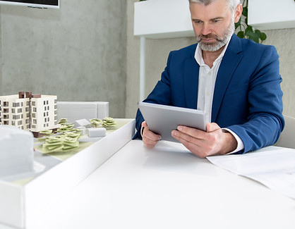 Executivo em traje formal usando tablet ao lado de maquete arquitetônica, ilustrando a aplicação da inteligência artificial da Leads Qualificados by InovaTech para identificar leads quentes e acelerar o fechamento de negócios imobiliários.