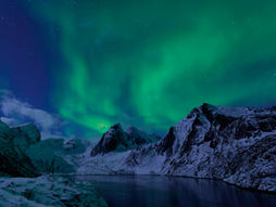 Auroras boreales verdes sobre las montañas cubiertas de nieve de las islas Lofoten en el Ártico de Noruega