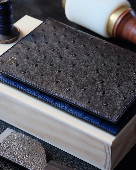 Atelier Decoster lange portemonnee nr. 60 in zwart struisvogelleer, binnenkant in lazuli geitenleer, marineblauw linnen draad en initialenmarkering in echt 22k goud. Ontworpen voor minimaal 12 kaarten, uw tickets, uw documenten, maar ook uw paspoort, dat volledig in een van de twee vakken onder de kaarten past. De ideale metgezel voor wie alles mee wil nemen.