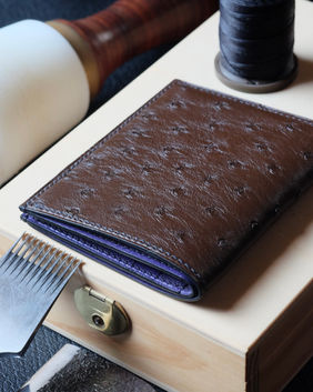 Portefeuille no. 31 entièrement fait main et cousu main en cuir d’autruche marron chocolat, intérieur en chèvre Sully violet, fil de lin noir, peinture des bords noire et initiales marquées à chaud.