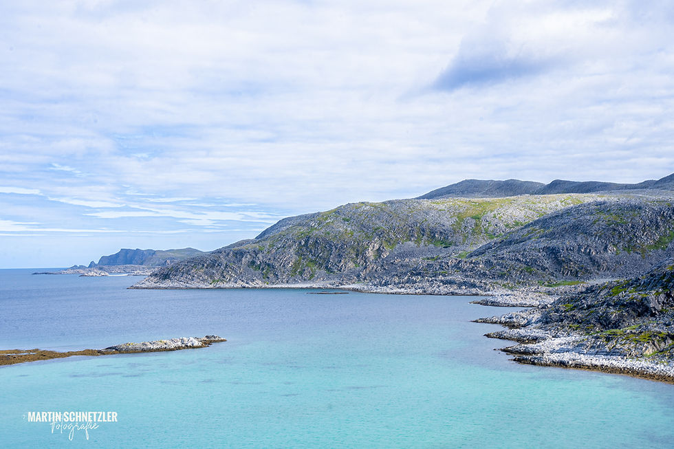 Turquoise sea against a rocky coast under a cloudy sky in Norway