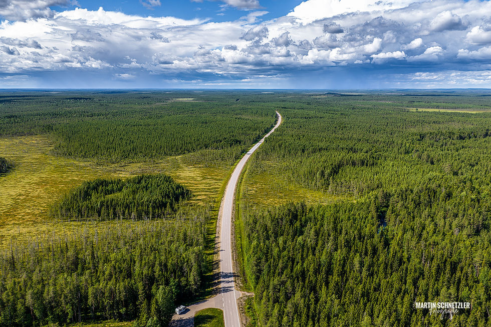 Aerial view: Narrow road through endless forest and moorland under a dramatic cloudy sky in Finland