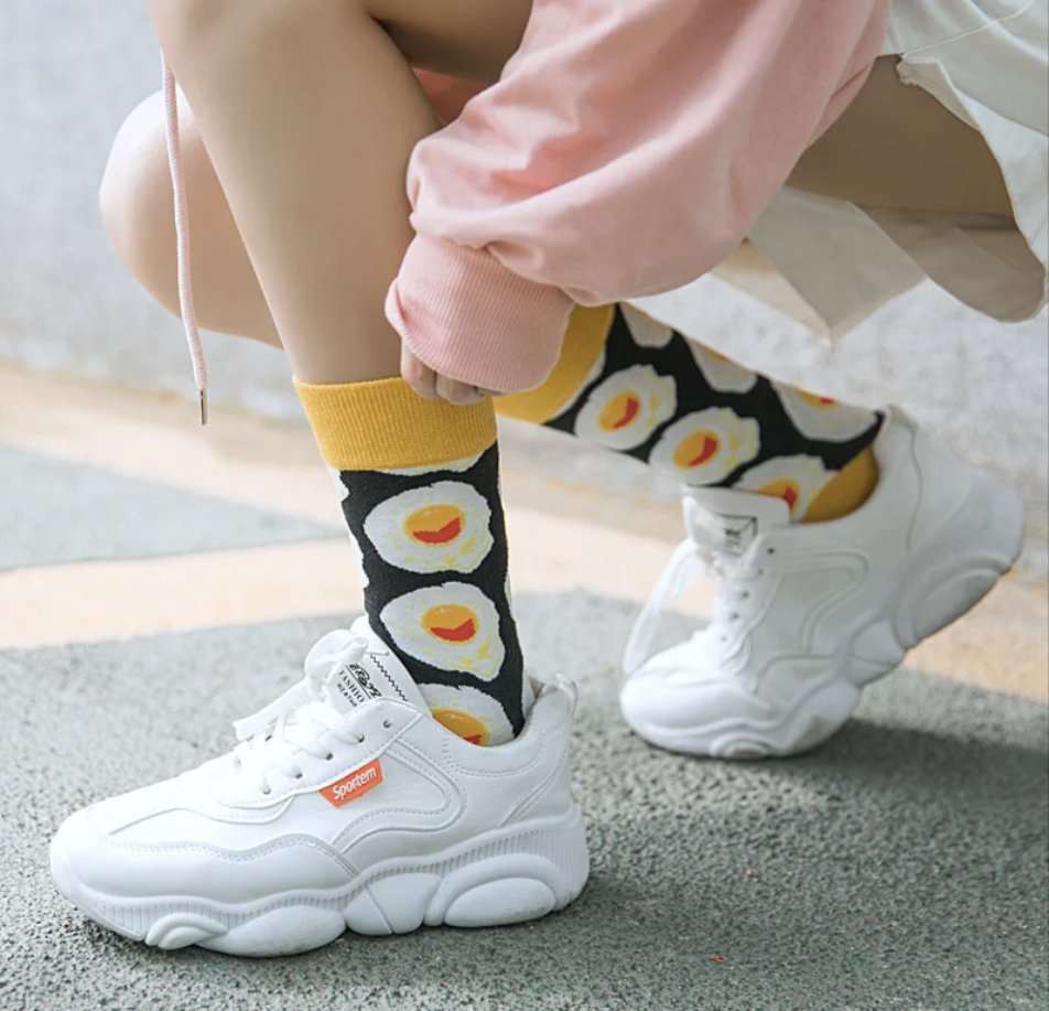 Person trägt schwarze Kawaii-Socken mit Spiegelei-Muster und weißen Sneakers – Streetstyle-Look.