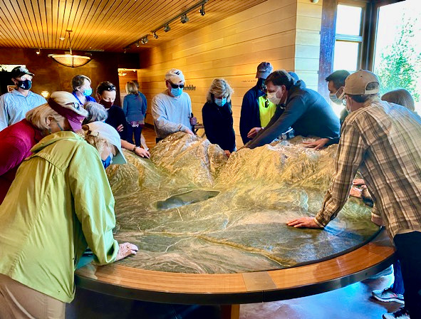Guests use their hands to get a feel of the Jackson Hole landscape represented on a large table size topographical map of the mountainous area.