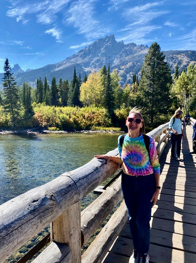 A guest poses in the sun on a footbridge traversing a bright lake in front of the mountains in Jackson Hole