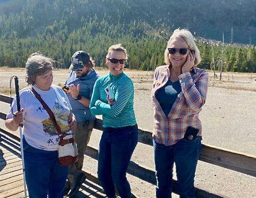 Four guests stand smiling on a sunny breezy day in the mountains