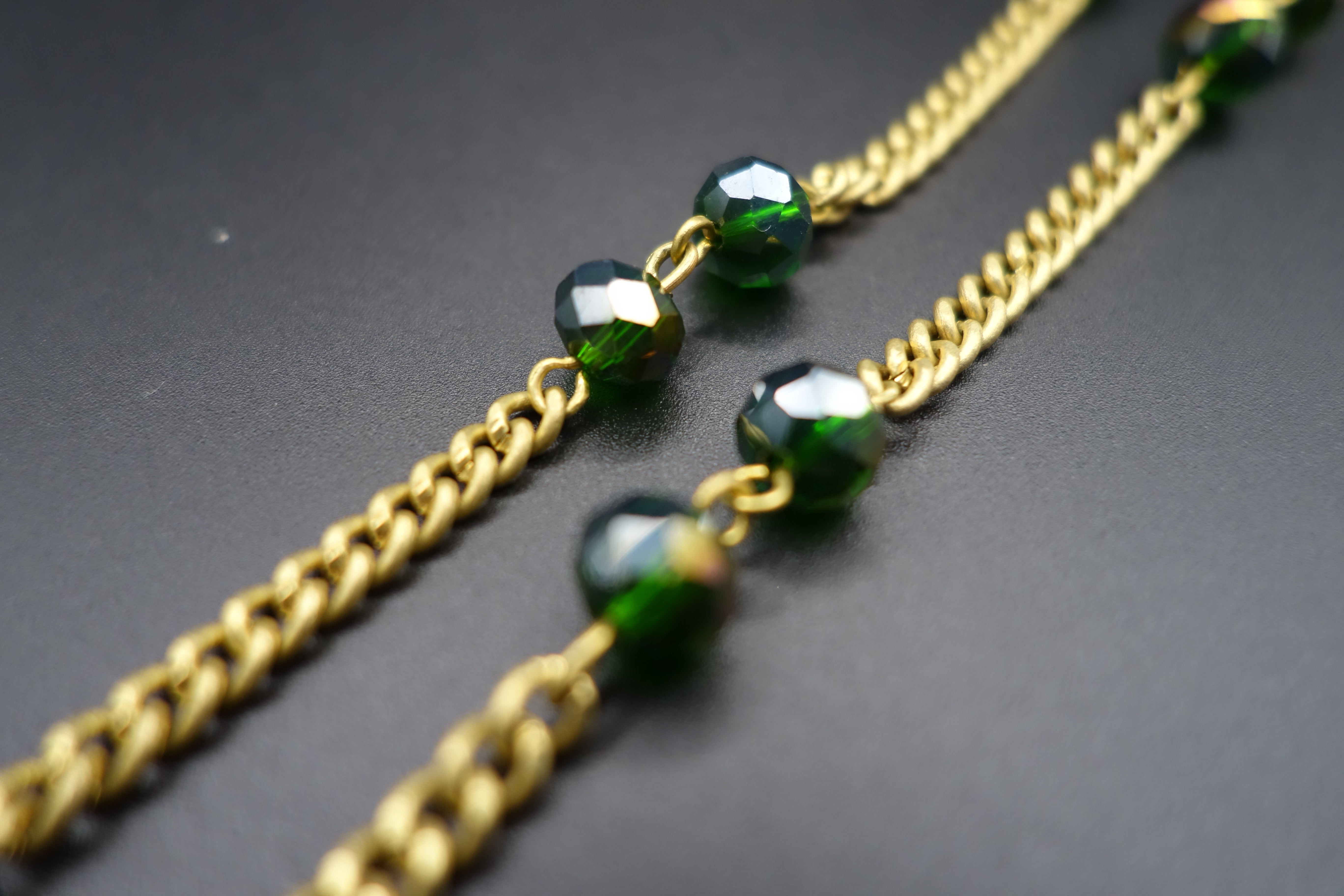 Close-up of gold chain necklace with green crystal beads on black background