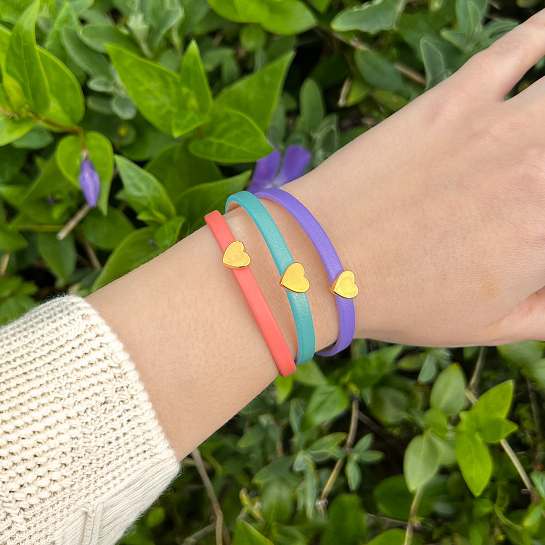 Model wearing three leather bracelets in coral, mint and lilac with a gold heart charm