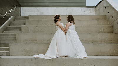 Two brides holding hands, looking at each other in an urban setting