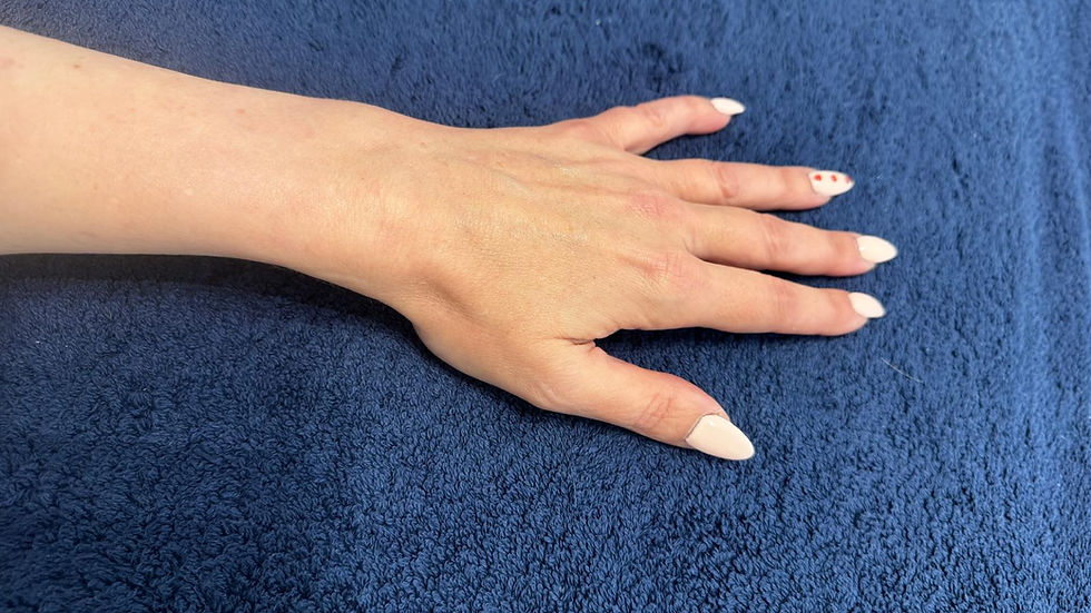 A hand with light pink nails, one with red dots, rests on a dark blue textured surface. Calm setting, natural lighting.