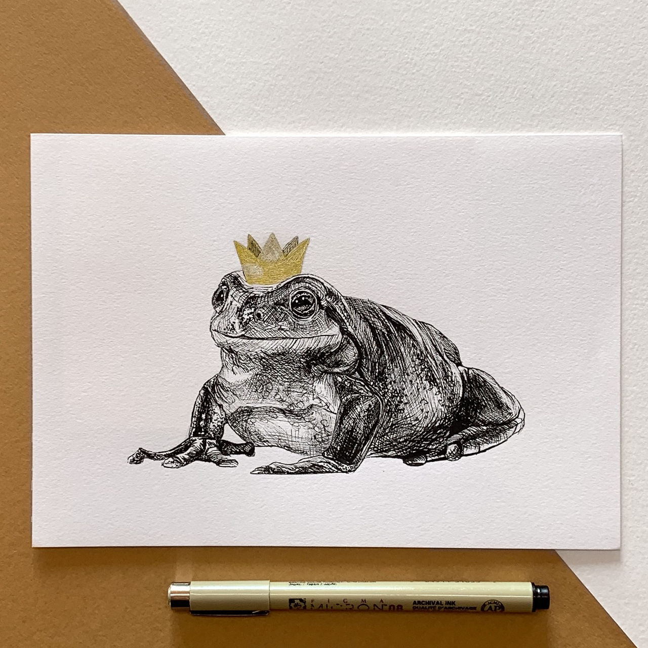 Ink drawing of a frog wearing a crown. The frog has been drawn with a fine liner pen and the crown has been coloured with golden ink. 