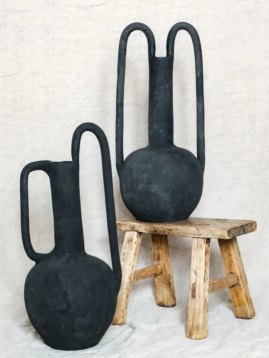 Deux grands vases noirs posés sur un tabouret en bois rustique. Fond beige en tissu, ambiance sobre et élégante. Décoration Artisanale - Vase céramique fait main
