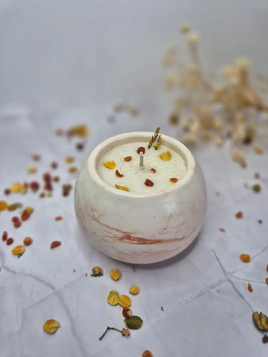 Bougie ronde blanche sur fond blanc, ornée de pétales jaunes et rouges, ambiance paisible et naturelle, herbes sèches en arrière-plan. Décoration intérieur artisanale