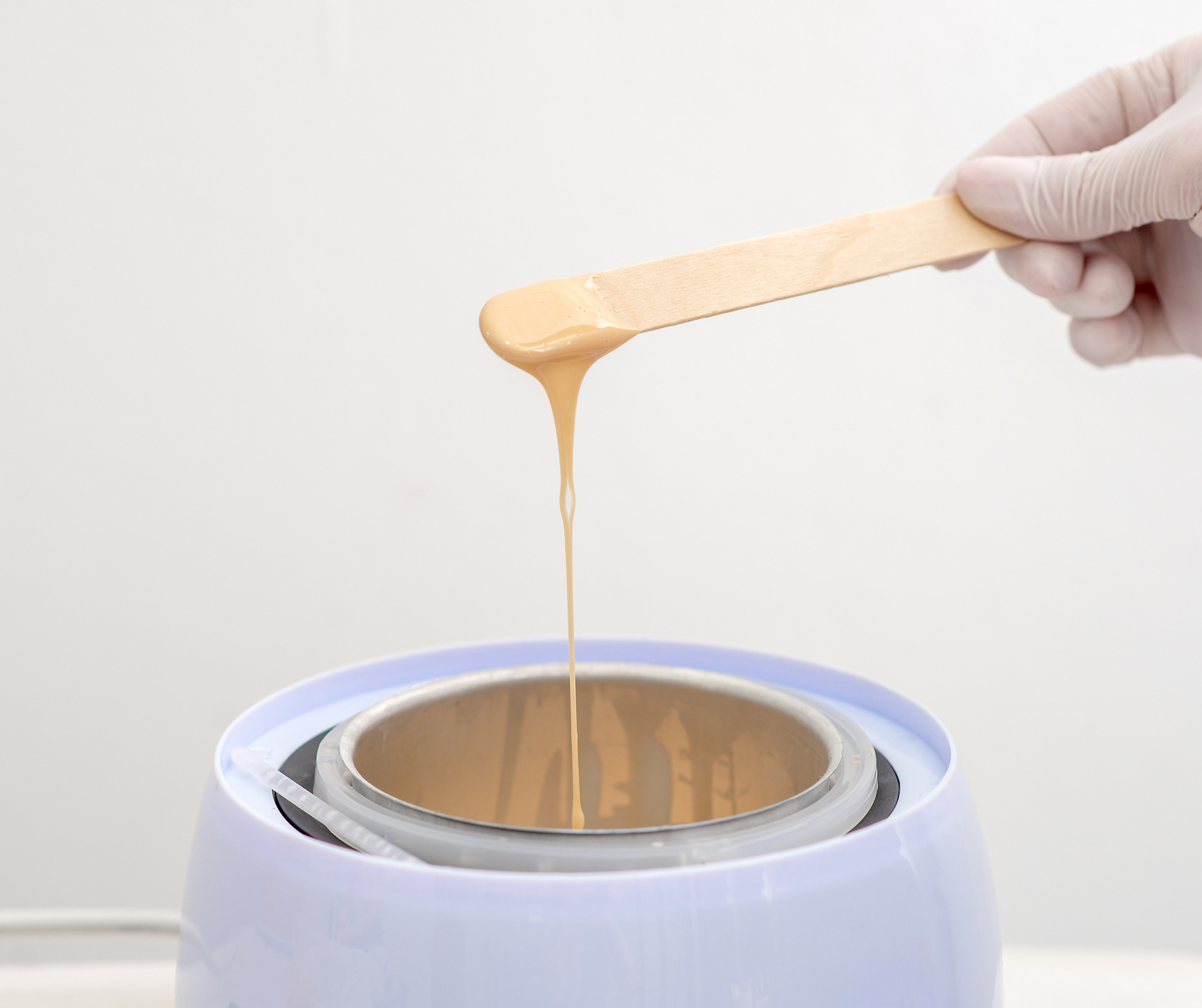 Golden wax on spatula drizzled into wax pot