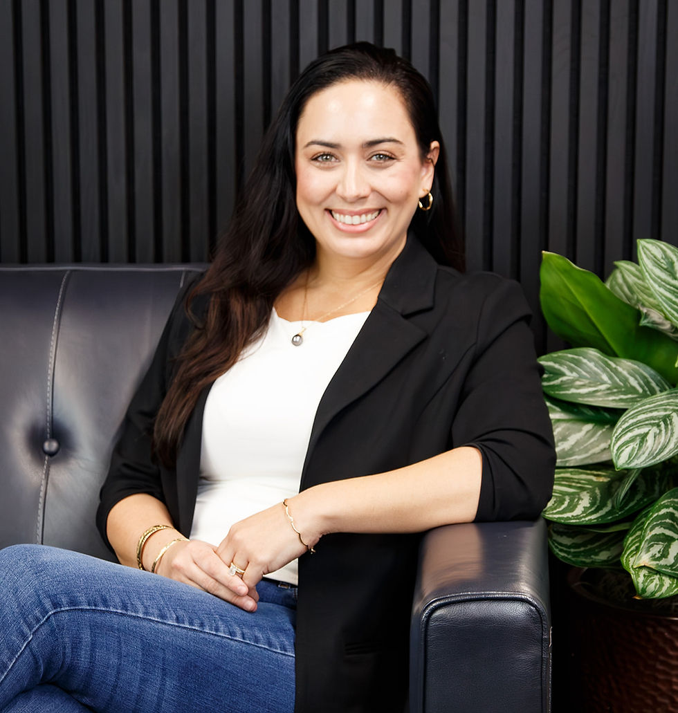 Samantha Schlegel a white lady with brown hair wearing a white top, black blazer, jeans, sitting on a black couch with black background.