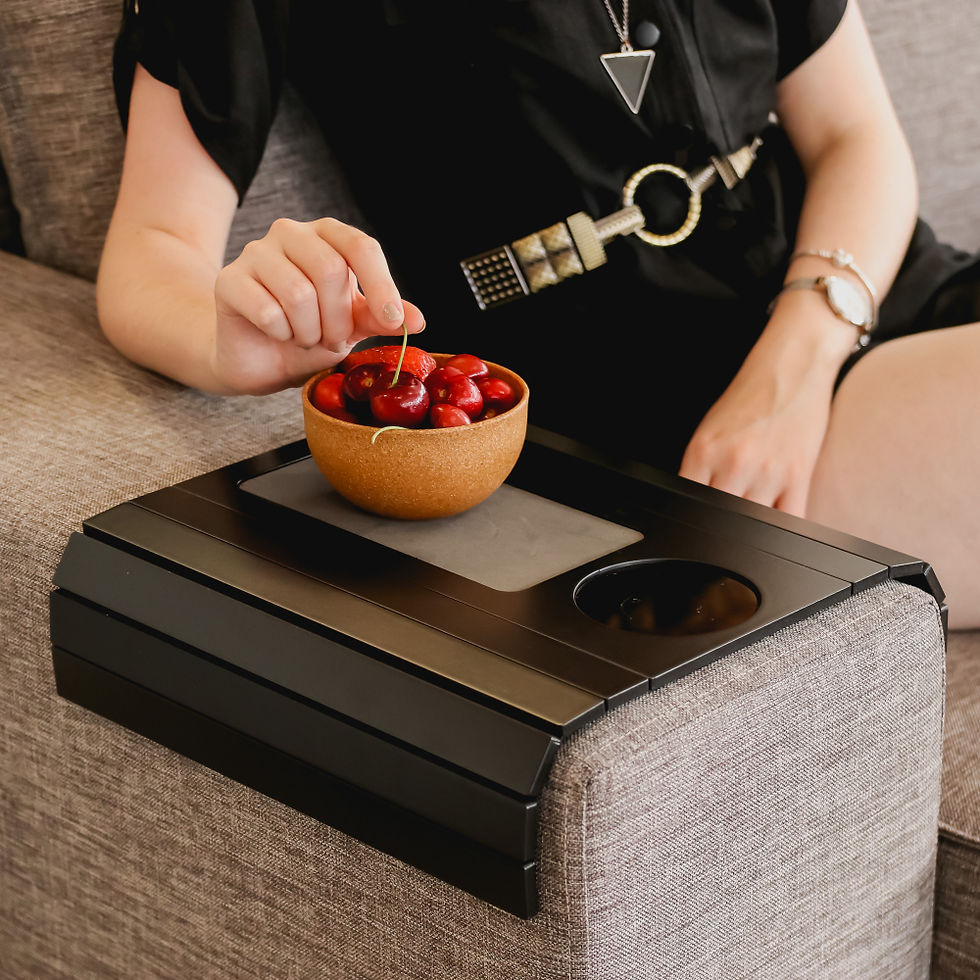 الصورة المصغرة: Side Vie of Sofa Mate Arm Tray Table tobacco color displayed on a Sofa Arm with model eating snacks.