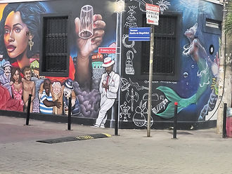 Una calle de Salvador da Bahía. Un poste con un cartel con el nombre de Rua Basílio de Magalhães. Una pared con un dibujo de graffiti con imágenes de personajes tradicionales de la cultura brasileña.