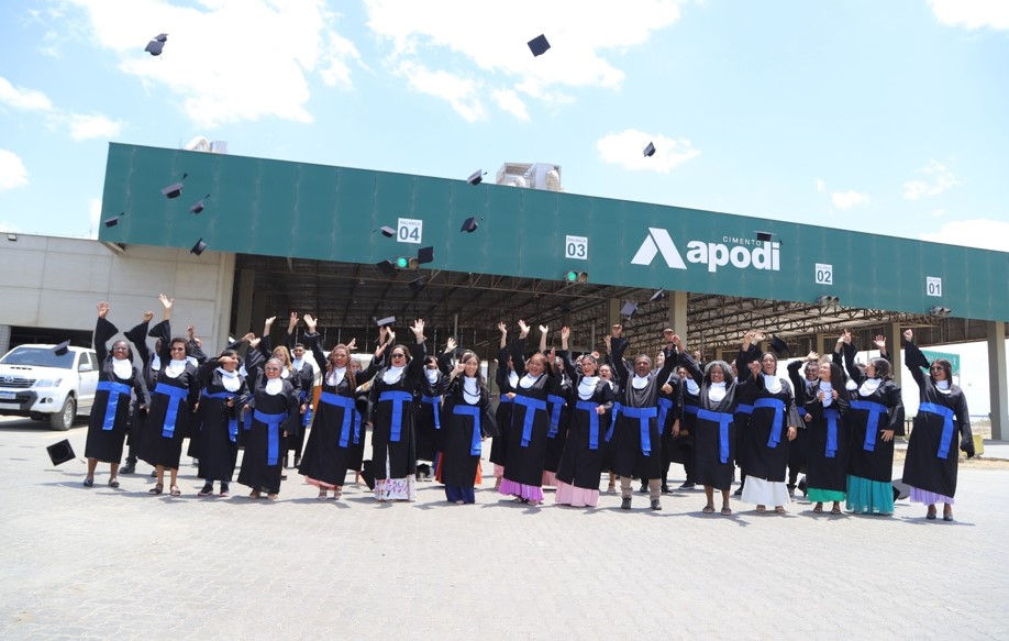 Grupo de estudantes usando beca comemoram jogando chapéus pra cima em frente a sede da cimento Apodi