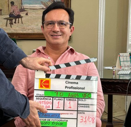 reitor da UFC Custódio Almeida usando camisa rosa segura claquete