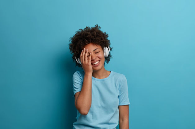 Pessoa negra, usando camiseta azul, ouvindo música com parede azul ao fundo