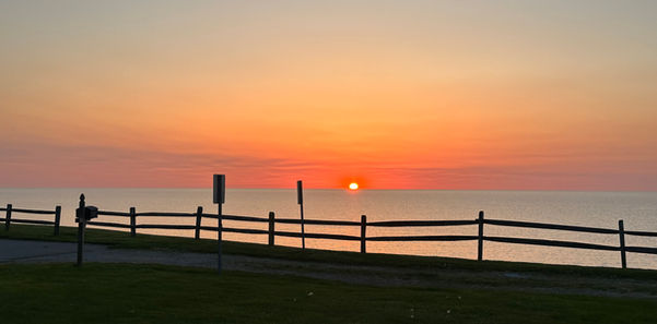 Orange sunset over the calm lake with a wooden fence in the foreground.