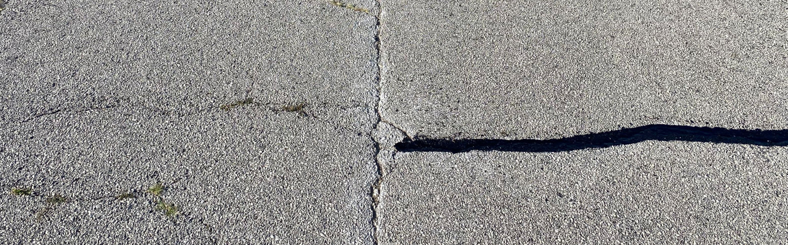 Cracked asphalt with a visible separation line, showing damage and wear