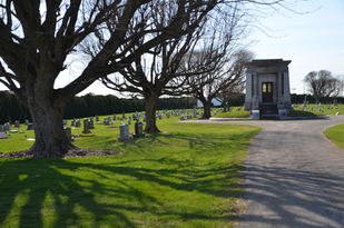 Grave yard with trees, pathway and monument, during a sunny day in Cedarville TWP.