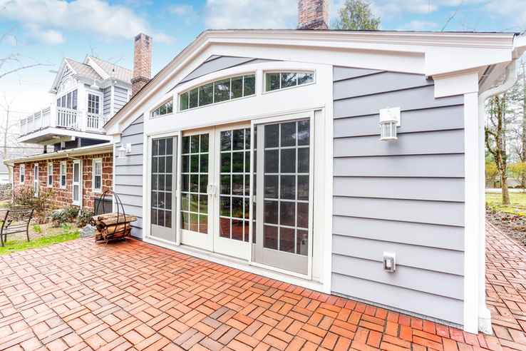 Luxury home addition in Rockland County featuring cement siding, custom trim, oversized glass doors, brick patio, and seamless integration with existing stone home architecture.