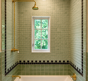 Custom bathroom renovation with handcrafted green tile walls, brass shower fixtures, integrated soaking tub, and natural light window by Peluso Construction in Rockland County NY.