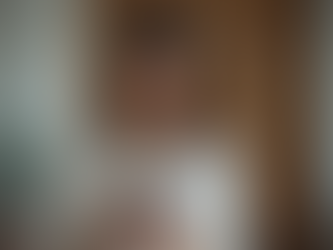 Woman in a white shirt smiling at her phone indoors, with a wooden door and potted plant in the background, creating a happy mood.