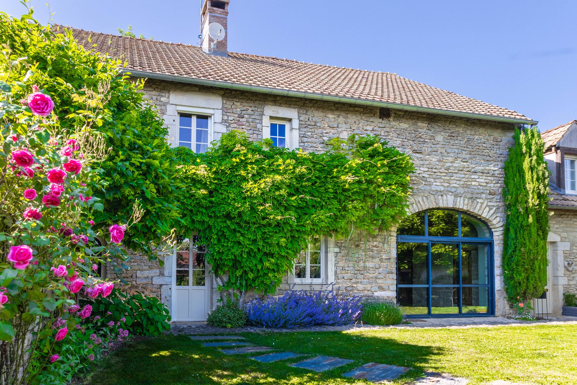 Façade en pierre de la Maison Coquelicots, glycine et rosiers en fleurs