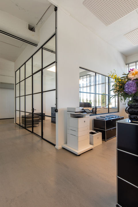 Offenes Office-Loft mit Bürogestaltung im Loftdesign mit Trennwänden aus Glas, unterteilt durch große Stahlgitter, die sich mit Drehtüren öffnen lassen. 